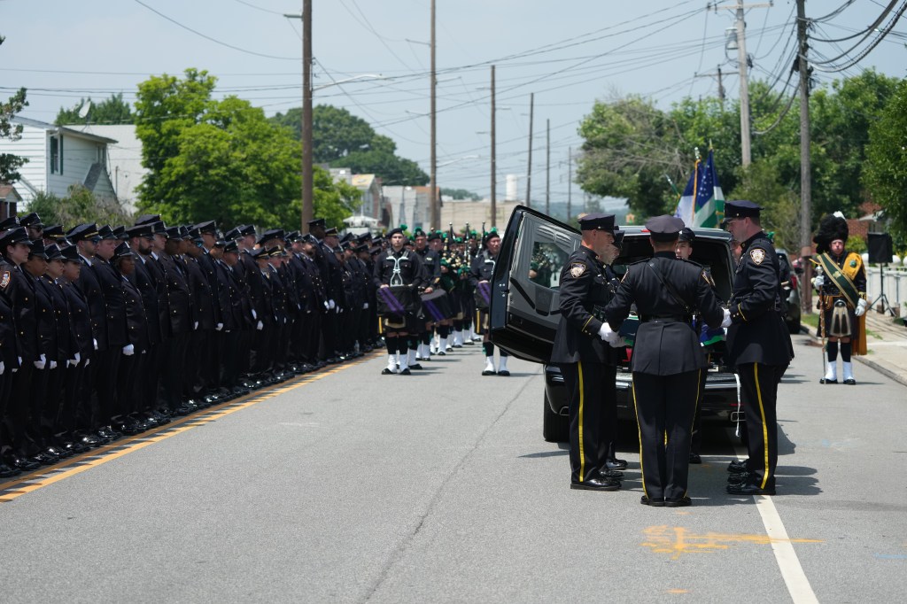 Photo shows uniformed police officers putting officer's casket into hearse.