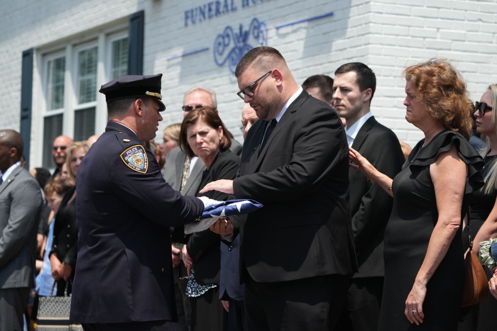 The heartbroken husband put his hand over the flag as he's comforted by family.