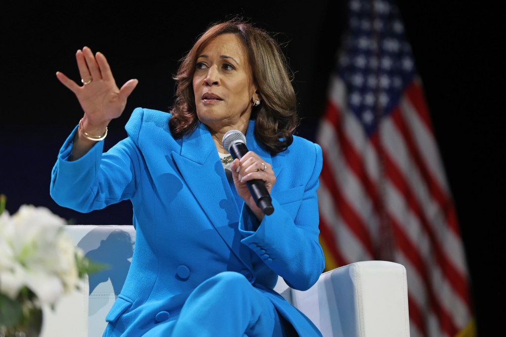 Kamala Harris in a blue suit gestures while holding a microphone.