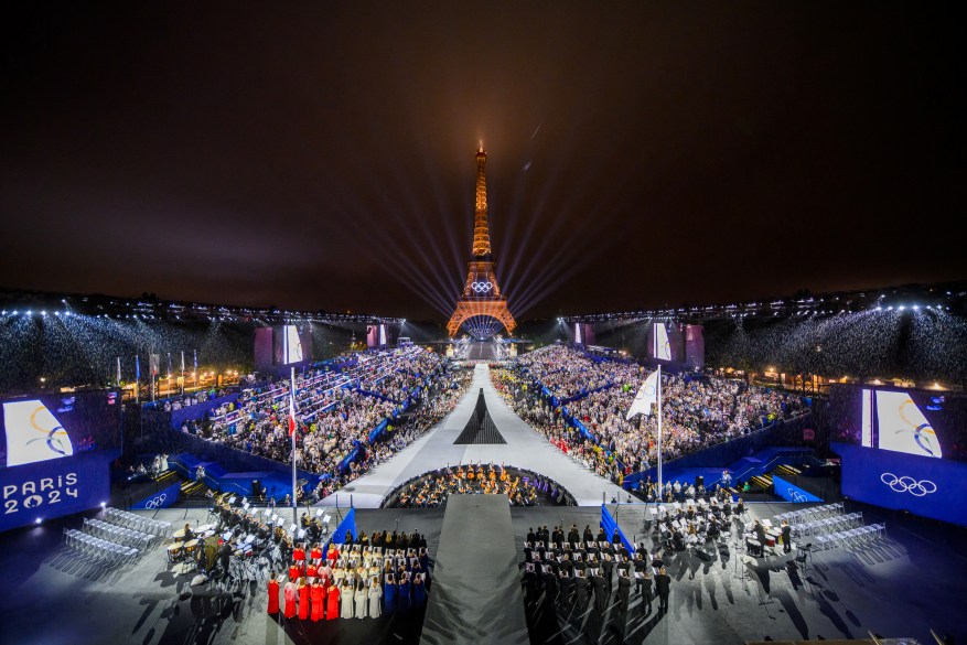 Overview of the Trocadero, with the Eiffel Tower looming in the background while the Olympic flag is raised during the opening ceremony.