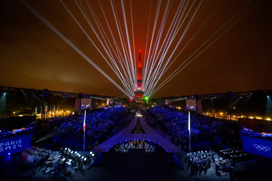 Overview of the Trocadero, with the Eiffel Tower looming in the background while the Olympic flag is raised during the opening ceremony.