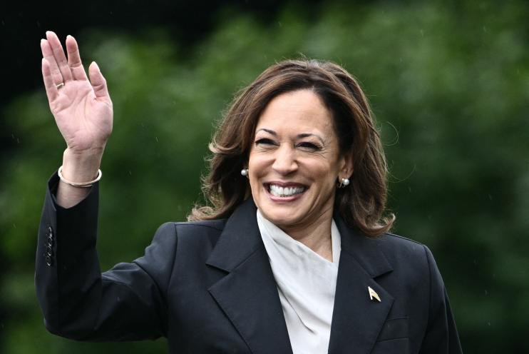 US Vice President Kamala Harris arriving at an event to honor NCAA championship teams at the White House, smiling with her hand up