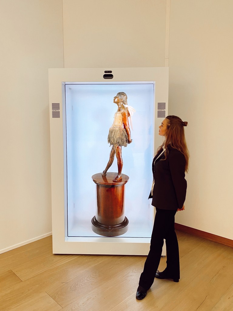 A woman observing a Degas hologram inside a glass display case