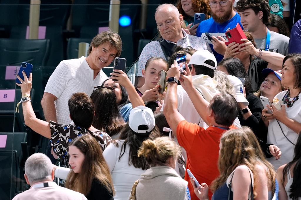 Actor Tom Cruise in white clothes posing with fans at the women's artistic gymnastics qualification round at the 2024 Summer Olympics in Paris, France