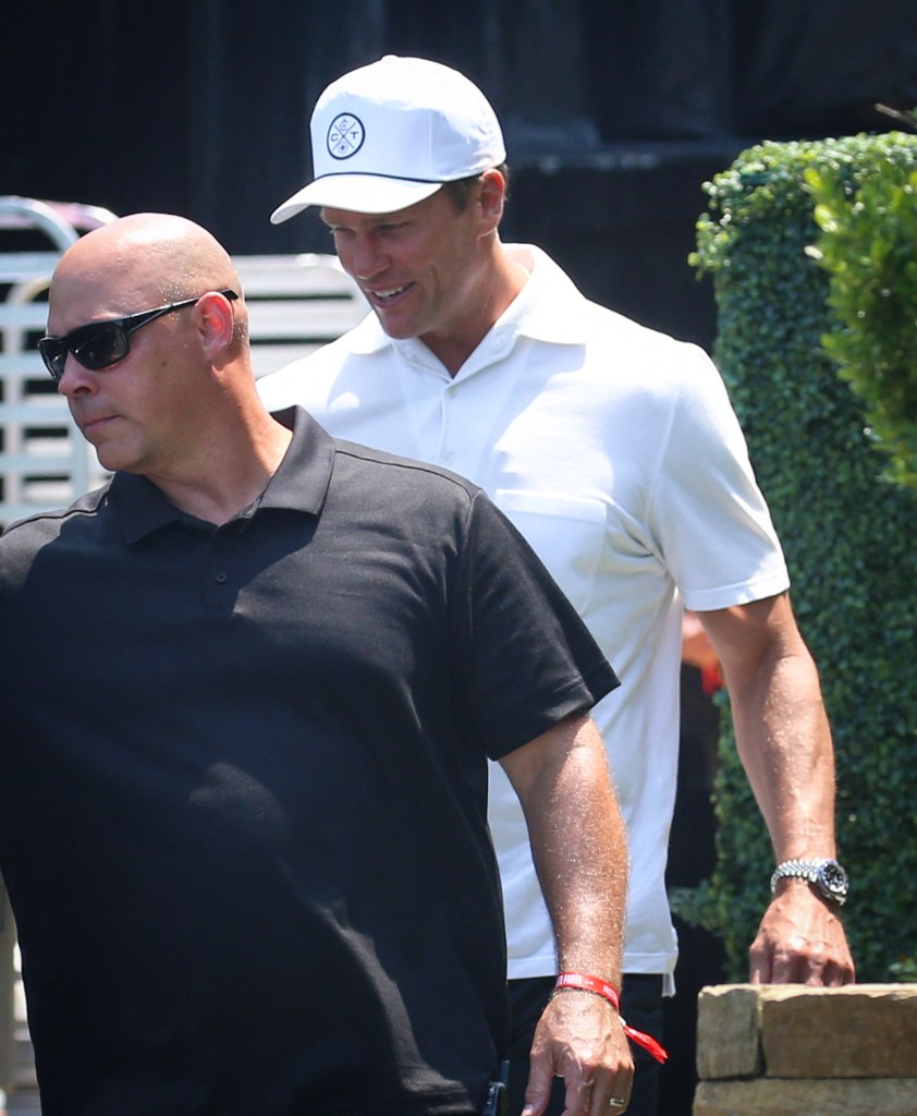 Tom Brady walking outside on a sunny day, wearing a Batman Rolex, while going to pick up a white outfit in Bridgehampton, New York