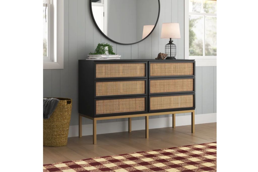 A 6-drawer dresser with dark wood in beneath a round mirror.
