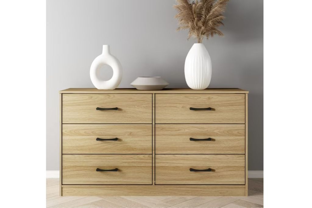 A light wood dresser with white vases on top.