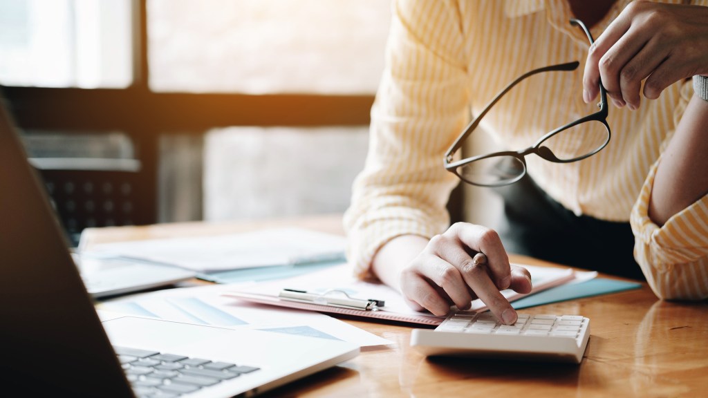 Business woman using a calculator and laptop for financial tasks on a wooden office desk