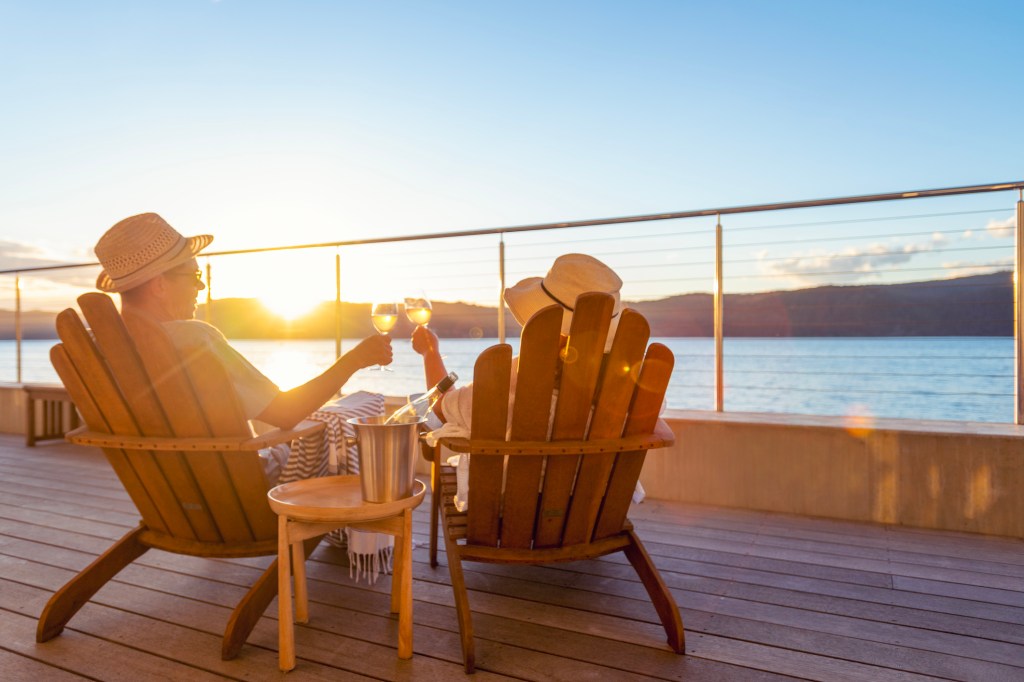 Couple relaxing on deck chairs, toasting with wine in an over water bungalow, enjoying the view
