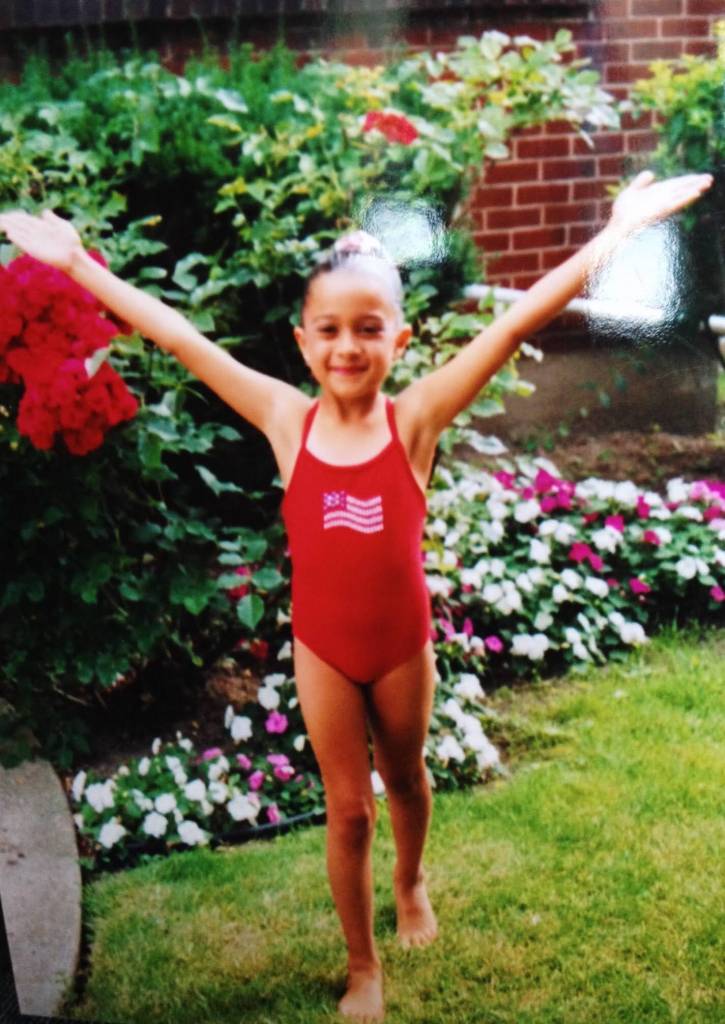 Anita Alvarez as a young girl in a red swimsuit posing with her arms out.