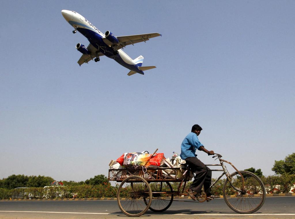 An IndiGo Airlines aircraft preparing to land as a man pedals his cycle rickshaw on the ground in Ahmedabad, India