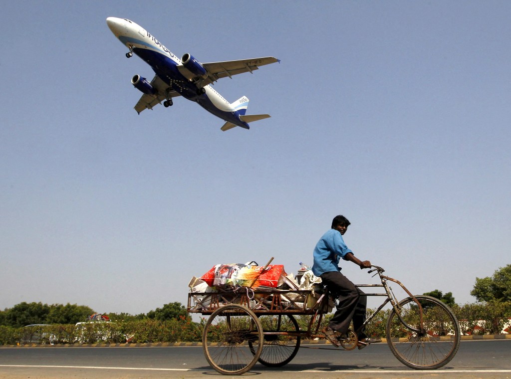 An IndiGo Airlines aircraft preparing to land as a man pedals his cycle rickshaw on the ground in Ahmedabad, India