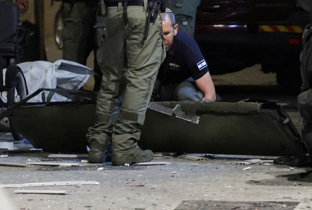 An investigator examines what, according to a police spokesperson, seems to be part of an aerial device, at the site of an explosion.