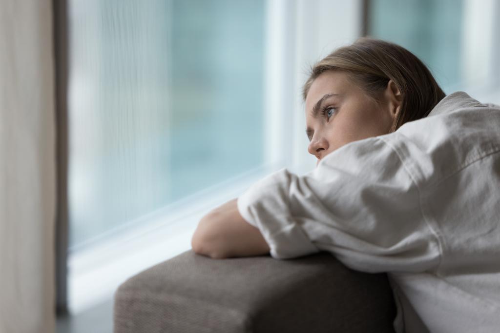 Lonely young woman lies on sofa, looking out window.