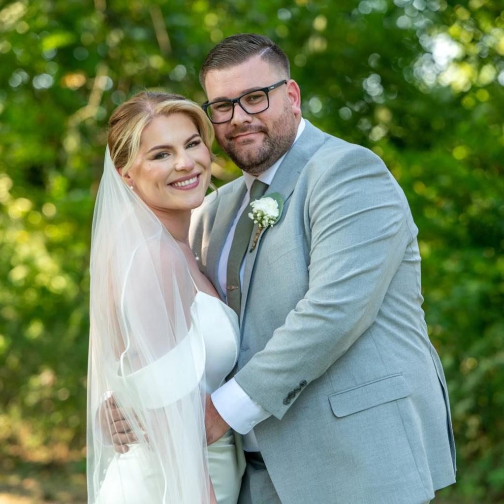 The husband wears a light blue suit and wife wears a white wedding dress.