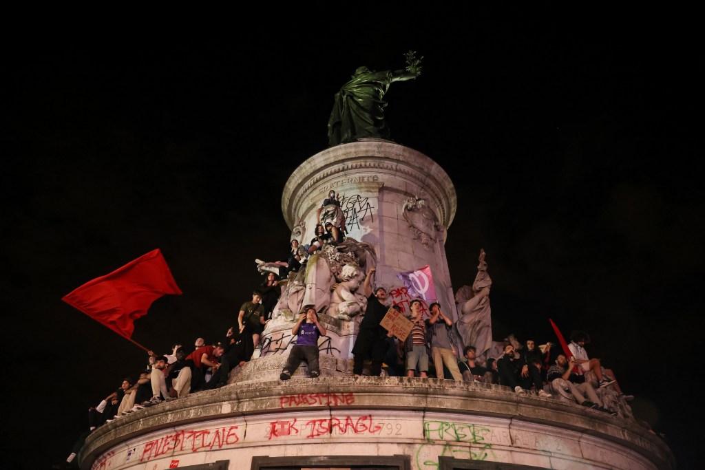 Graffiti on a large statue in Paris covered in demonstrators.