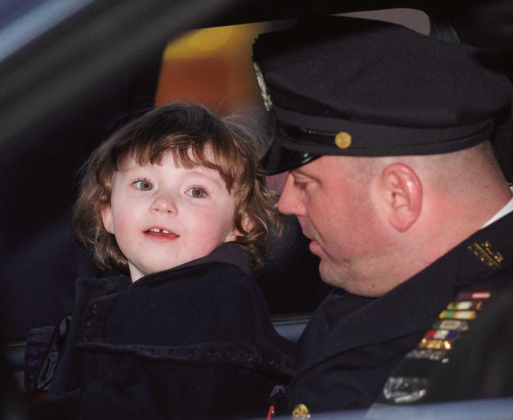 Patricia Mary Smith (2 years old) rests in the arms of her father, PO James Smith, after attending the funeral of her mother