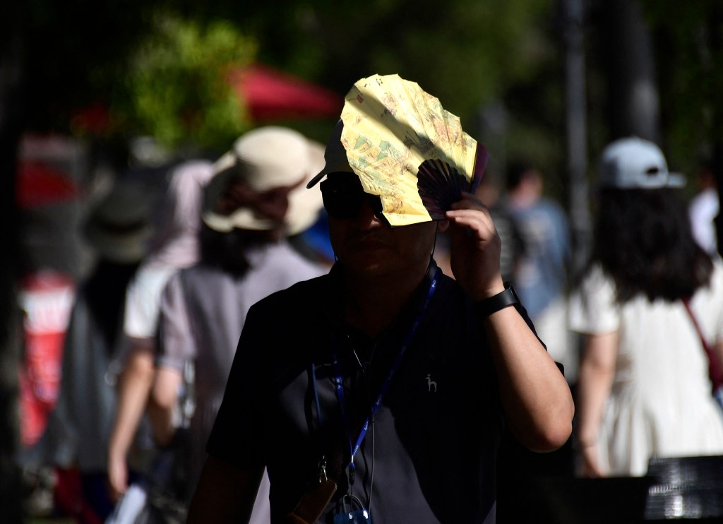 A tourist shielding himself from the sun with a fan while walking on a street in Seville during a heatwave.