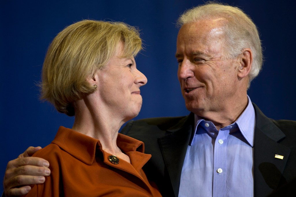 A man on the right smiles at the woman on the left side of the photo as they smile at each other. The man has his arm around the woman's shoulder. 