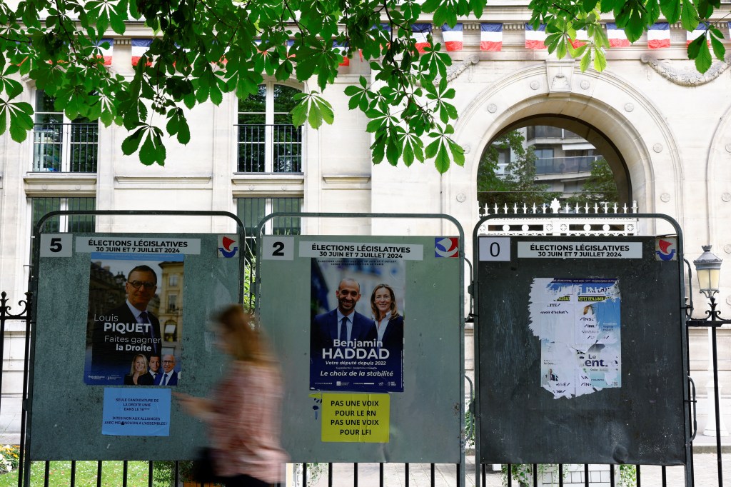 A woman walks past campaign posters on an election board prior to the second round of the early French parliamentary elections.