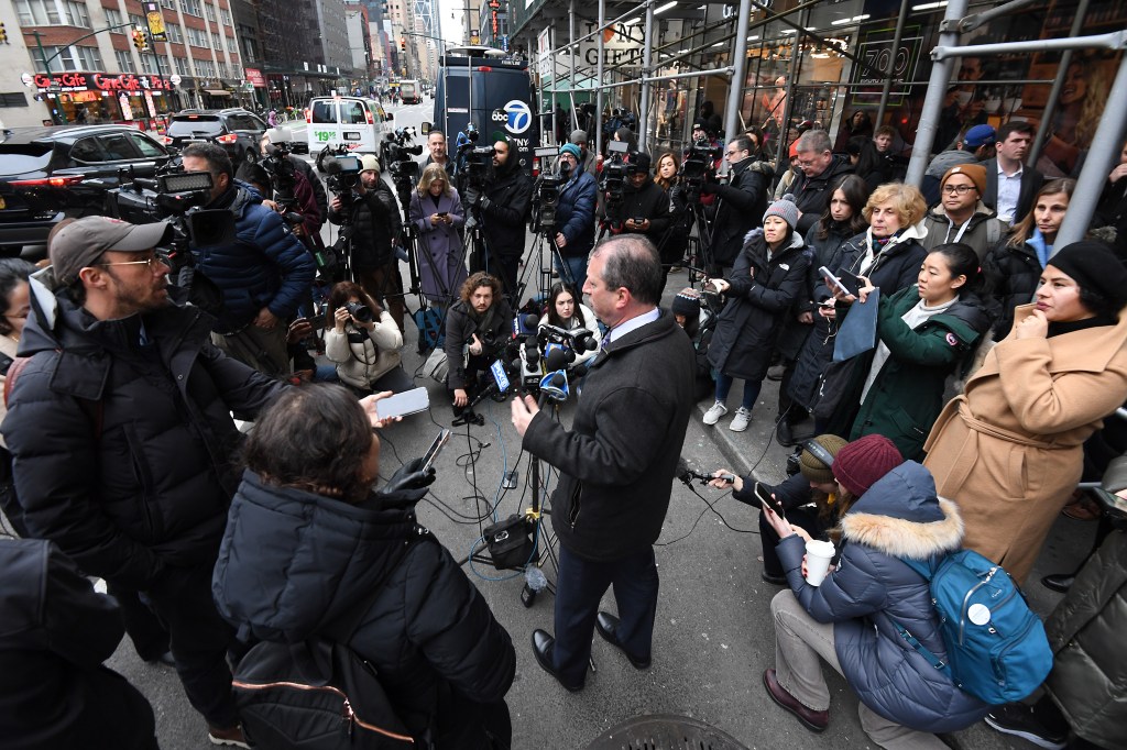 NYC Comptroller Brad Lander speaking at a press conference outside the Row hotel surrounded by crowd and microphones