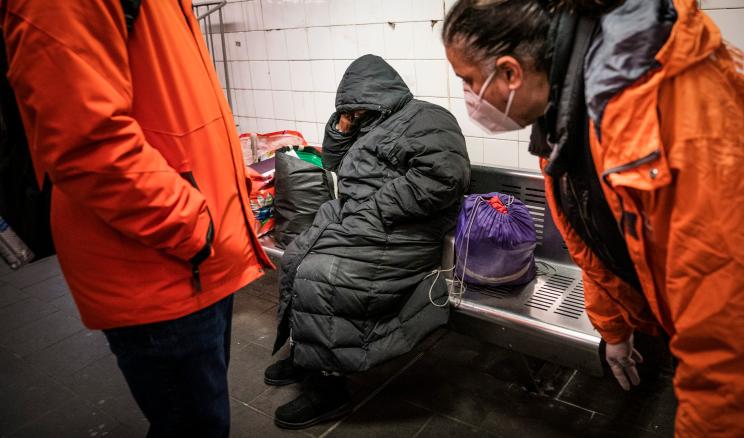 Workers with Homeless Outreach interact with a person sleeping on a bench in the Manhattan subway system, Monday, Feb. 21, 2022, in New York