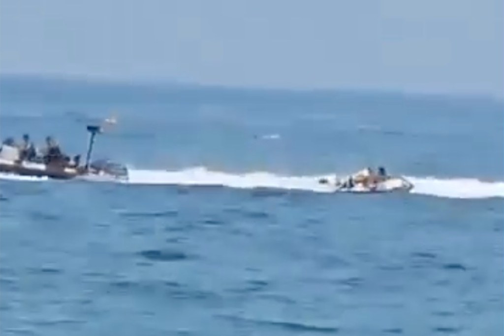 Spanish police boat veering towards a small inflatable dinghy carrying four individuals, resulting in one person falling into water