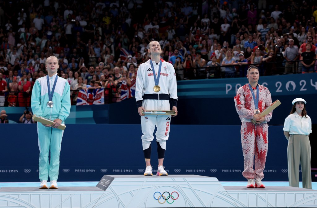 Bryony Page of Britain celebrating her gold medal victory on the podium, alongside silver medallist Viyaleta Bardzilouskaya of AIN and bronze medallist Sophiane Methot of Canada, at the Paris 2024 Olympics Trampoline Women's Victory Ceremony