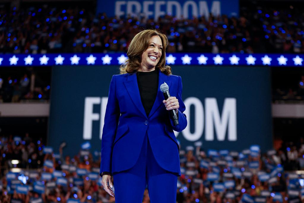 2024 Democratic presidential candidate Kamala Harris, in a blue suit, holding a microphone at a campaign rally in Milwaukee, Wisconsin.