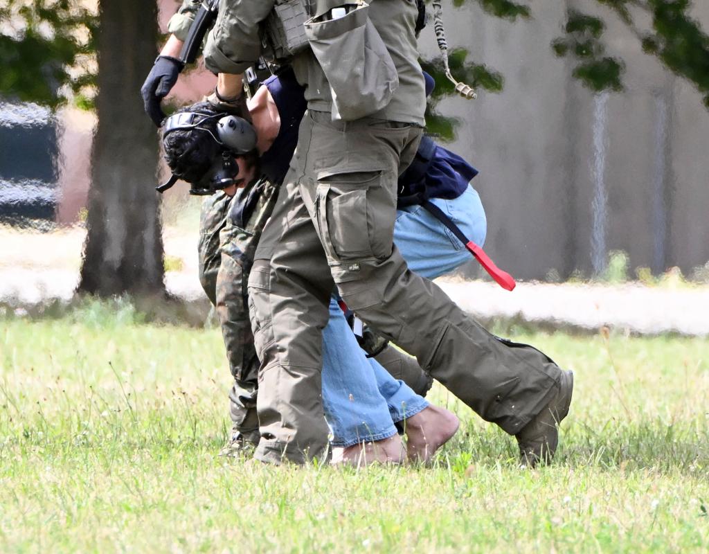 Police hold the man's head low to the ground as he wears blinders and headphones. 