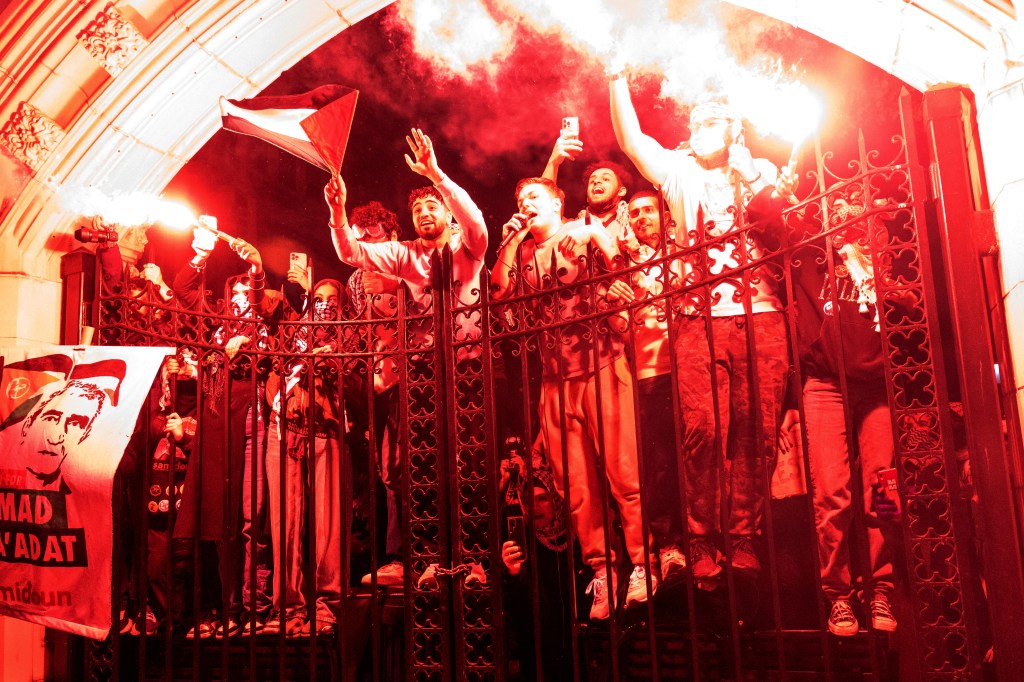 Protesters stand in an archway bathed in a red light from a flare.