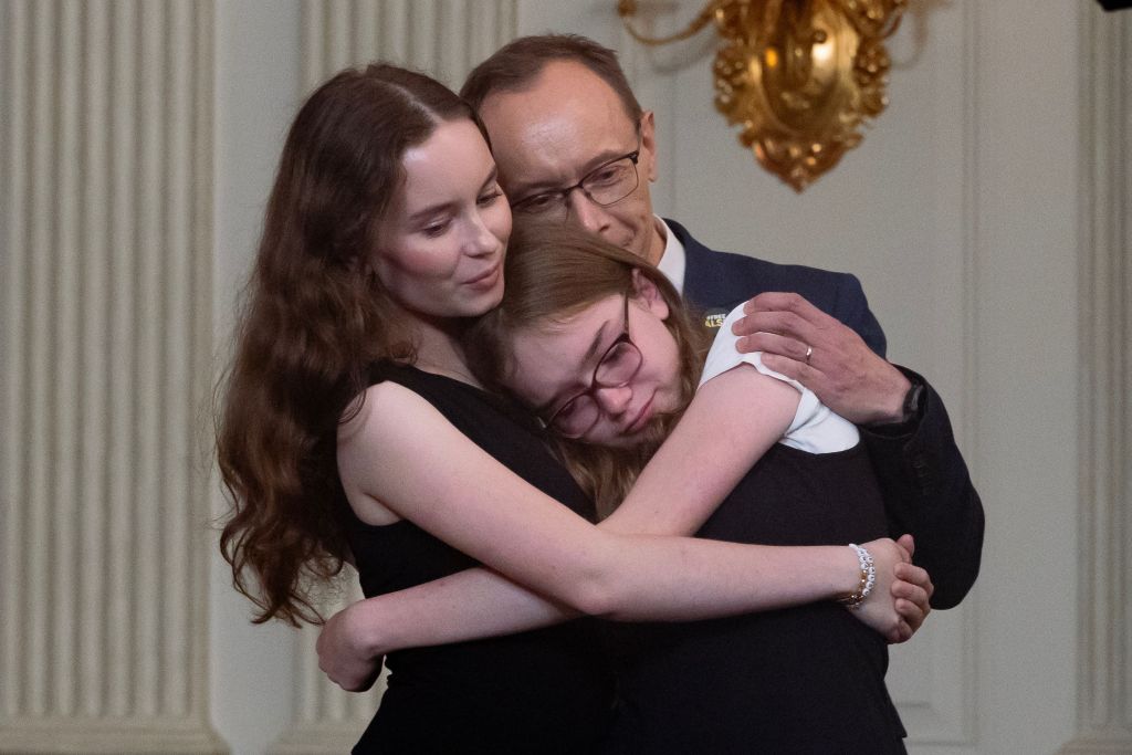 The family of Alsu Kurmasheva: husband Pavel Butorin (Back), daughter Miriam Butorin (R) and daughter Bibi Butorin (L) embrace while listening to US President Joe Biden speaking on a prisoner swap with Russia, in the State Dining Room of the White House in Washington, DC.