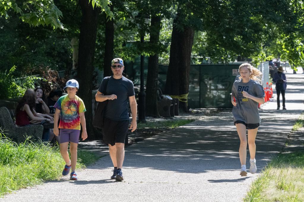 A woman jobs through Prospect Park, passed a father and son walking.