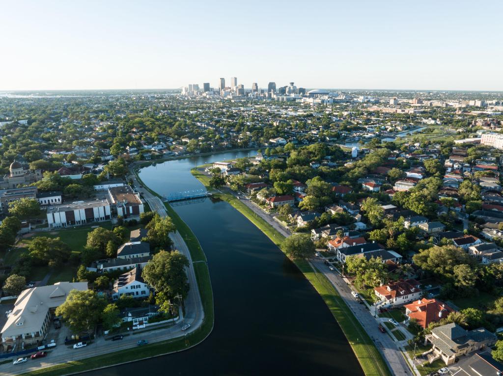 Aerial view of the historic Bayou St. John winding through a lush New Orleans neighborhood, with the city skyline visible in the distance