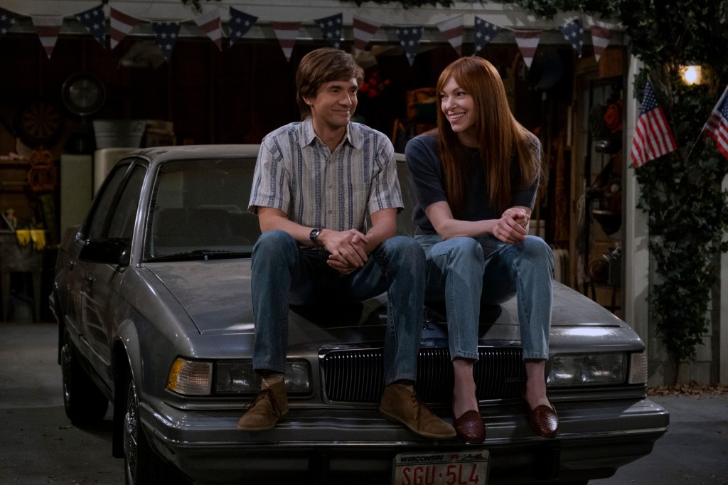 Topher Grace as Eric Forman, Laura Prepon as Donna Pinciotti smiling together on a car. 