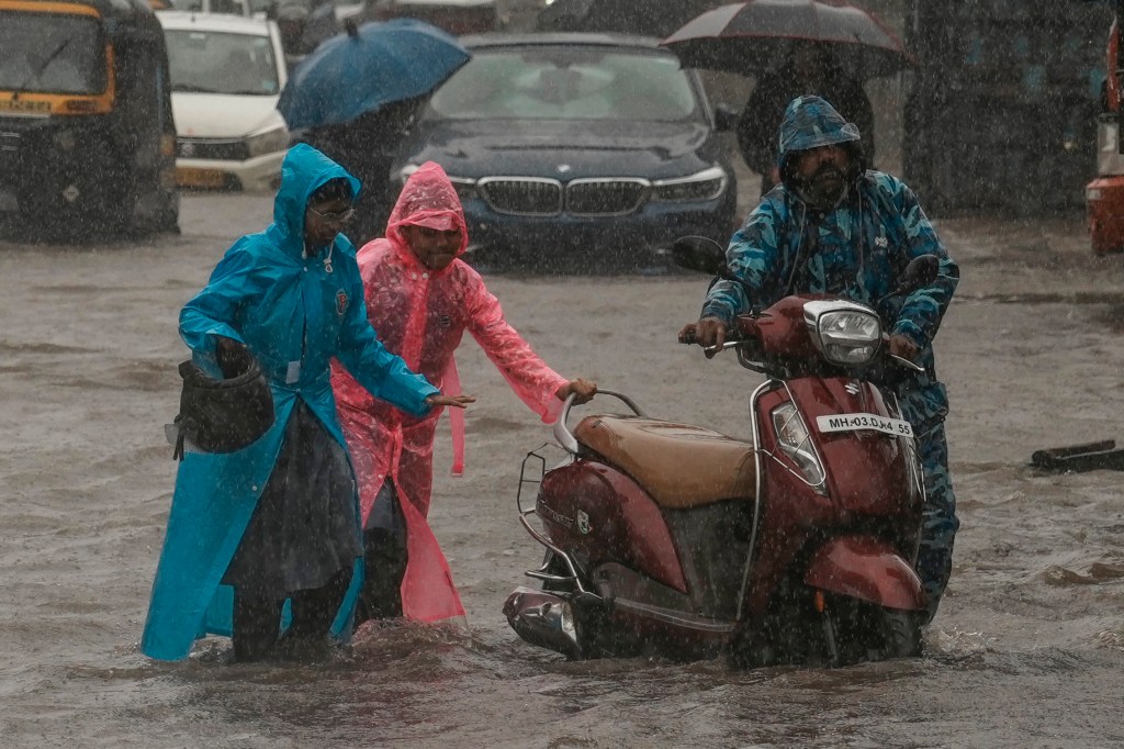  Children push their father's scooter through a flooded street as it rains in Mumbai, India, on July 25, 2024. 