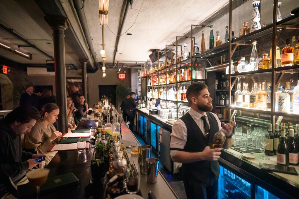 Karen Akerman in the lower level dining room of Tucci NYC, an Italian restaurant in Manhattan, New York City, with a man holding a bottle in the background