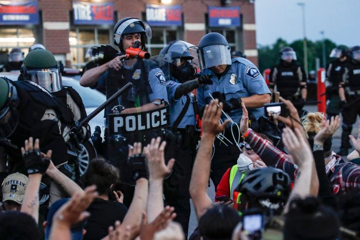 A police officer covers protesters who have been detained pending arrest on South Washington Street in Minneapolis, May 31, 2020.