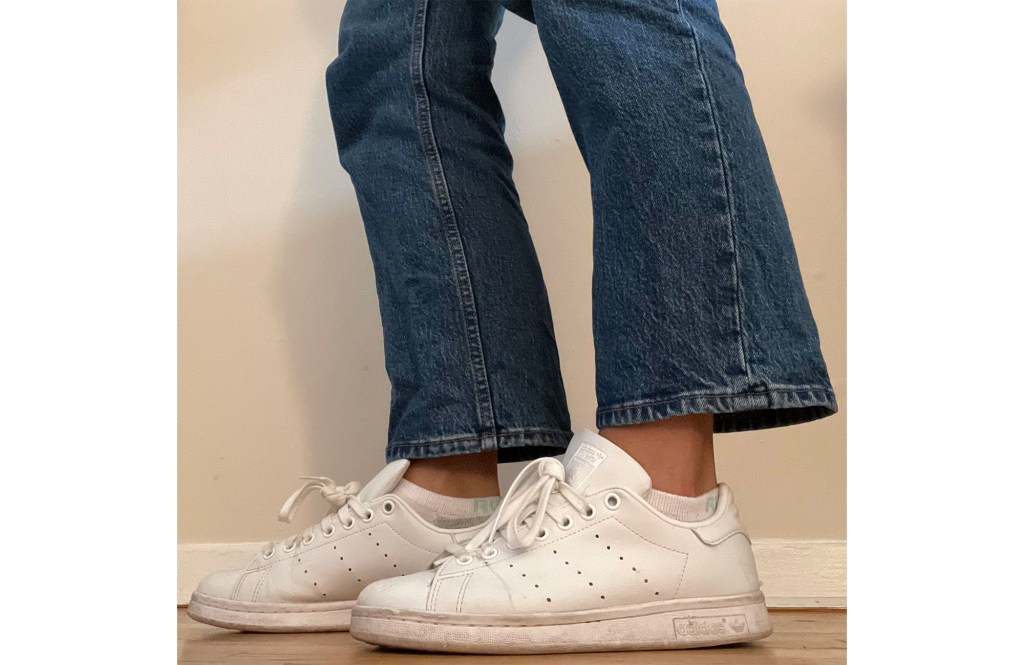 A person's legs and feet wearing white shoes