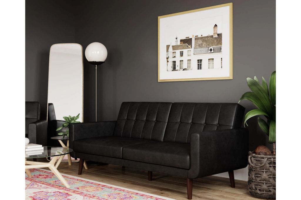 A black faux leather couch that converts into a futon in a living room.