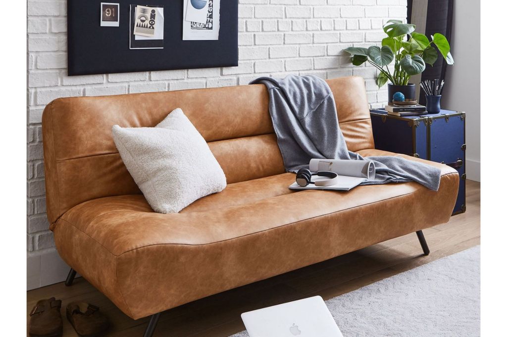 A faux leather couch in a stylish room with a white brick wall.