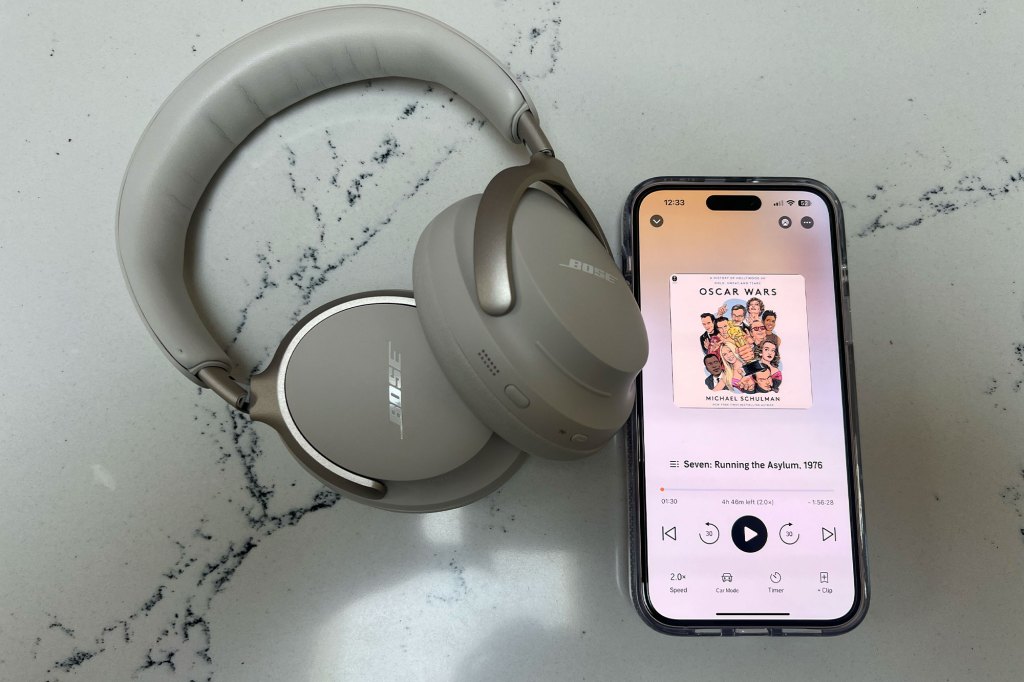 A phone displaying the Audible app alongside headphones on a marble surface