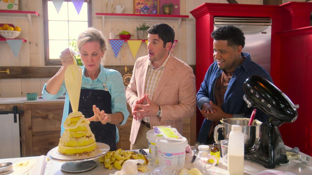 Jason Biggs in "Blue Ribbon Baking Championship" watching a woman frost a cake. 