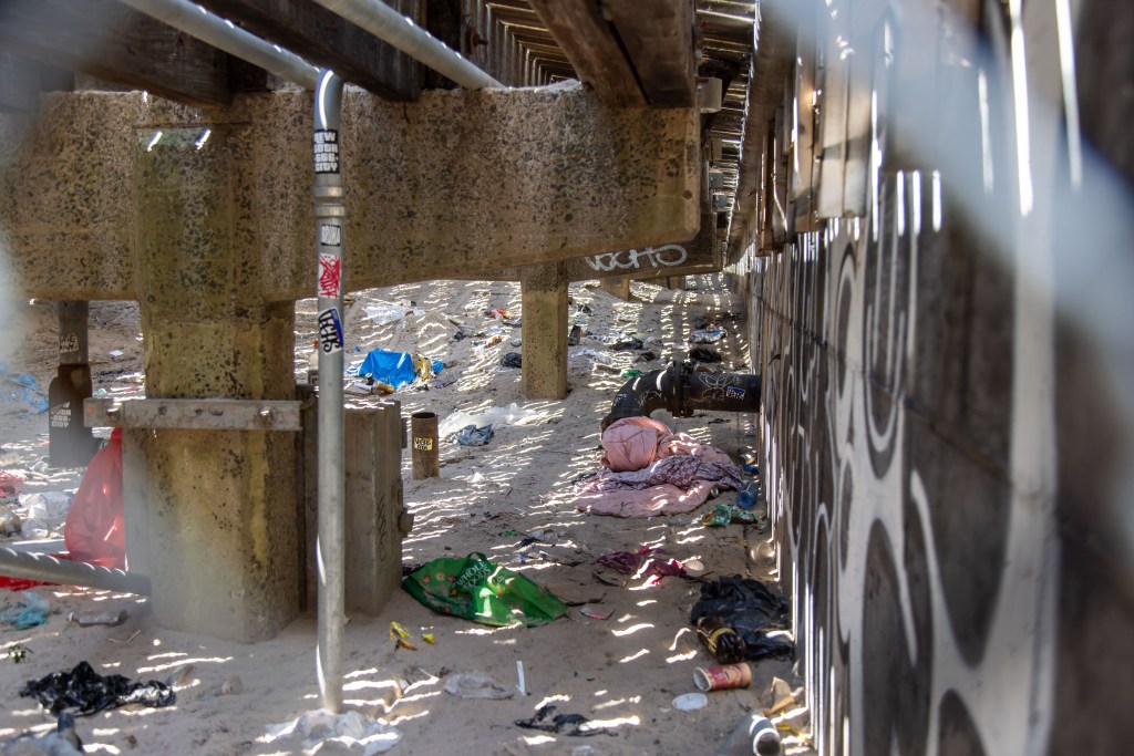 Discarded blankets, clothes and trash seen underneath the boardwalk.