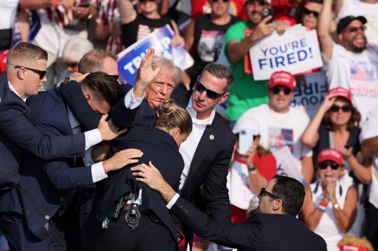 Republican presidential candidate and former President Donald Trump gestures with a bloodied face while he is assisted by U.S. Secret Service personnel after he was shot in the right ear during a campaign rally at the Butler Farm Show in Butler, Pennsylvania, U.S., July 13, 2024.