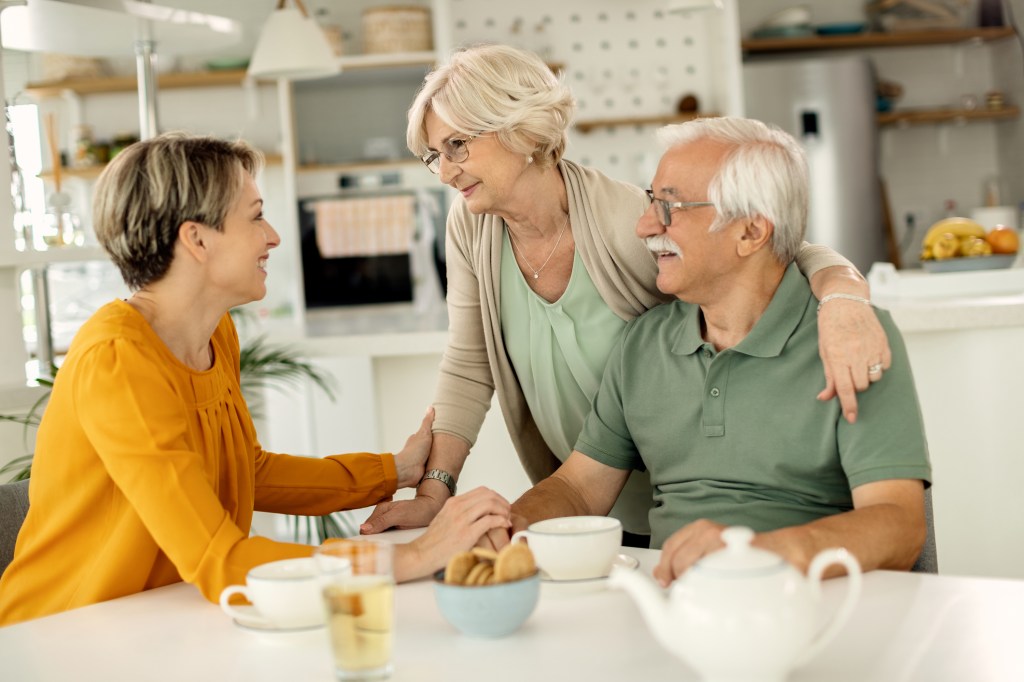 Happy mature couple engaged in conversation with their adult daughter visiting them at home