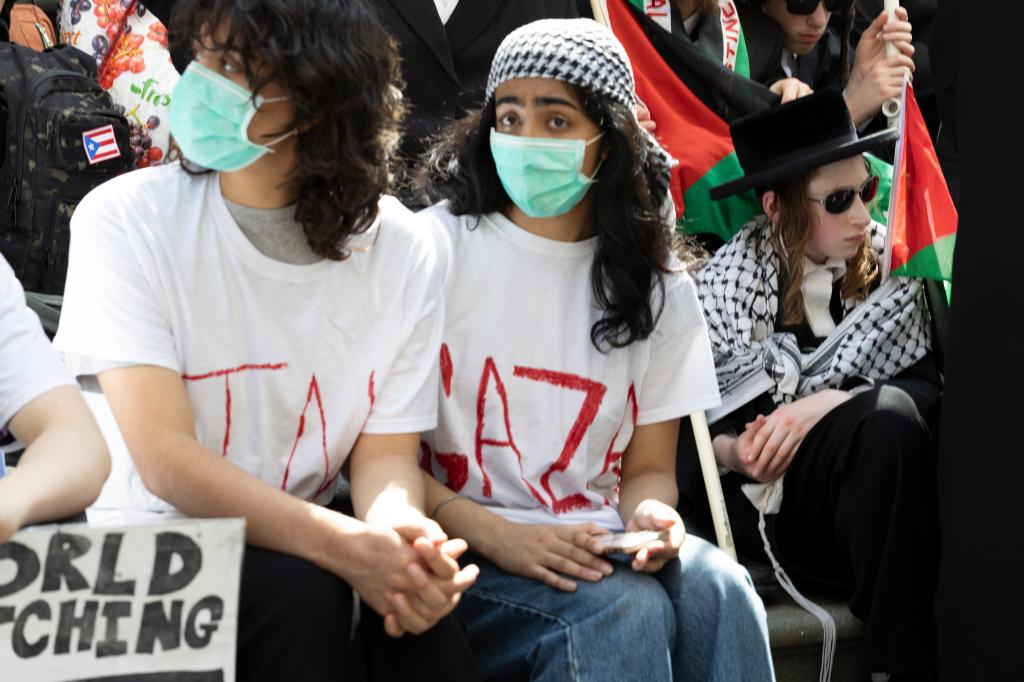 High school students rallying for Gaza on the steps of Tweed Courthouse, with a student wearing a 'GAZA' t-shirt and an anti-Zionist Jewish man in the background.