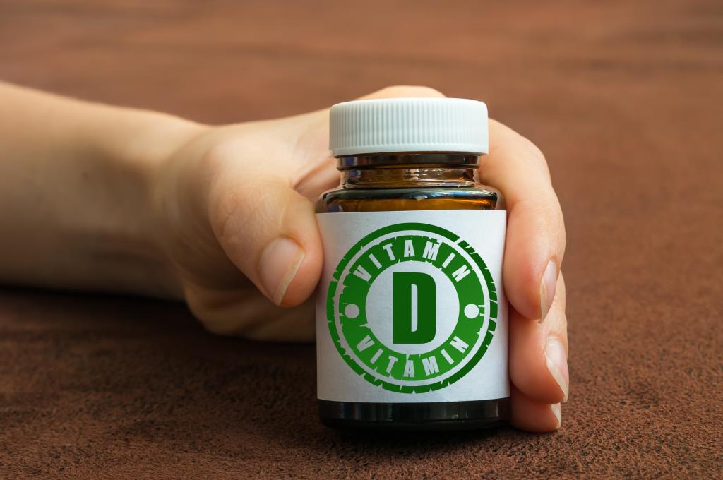 Human hand holding a bottle of Vitamin D pills on a brown background