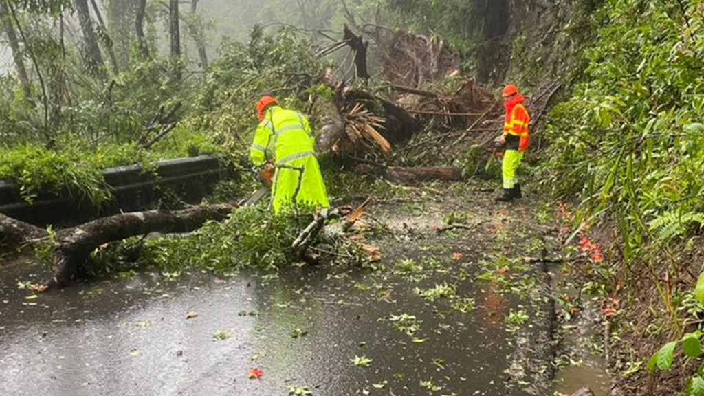 Hawaii Department of Transportation crews in yellow safety gear clearing debris from a landslide on Hana Highway near Upper Waikani Falls during Hurricane Hone