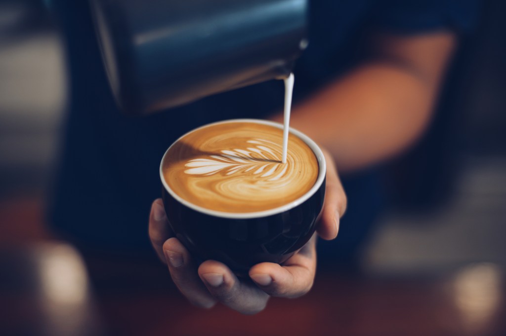 A person pouring milk into a cup of coffee to make latte art